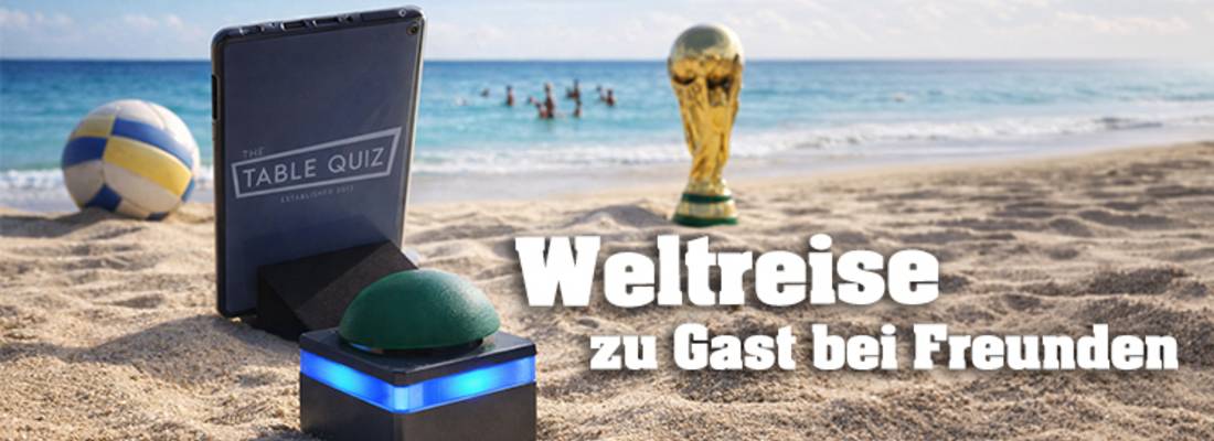 Tablet und Buzzer stehen am Strand vor dem Meer, im Hintergrund sind Menschen im Meer, ein Volleyball und der WM Pokal stehen am Strand