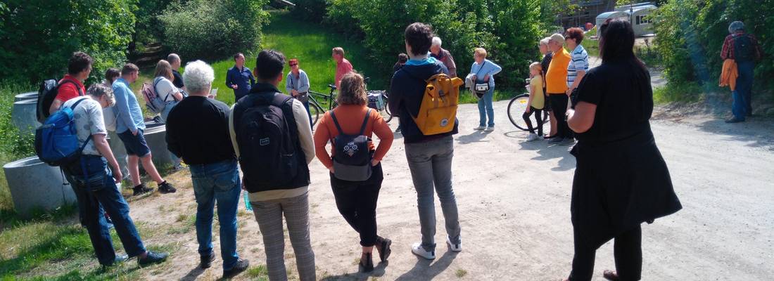 Eine Gruppe von Personen stehend im Kreis, die sich unterhalten. Im Hintergrund grüne Büsche und Gras.