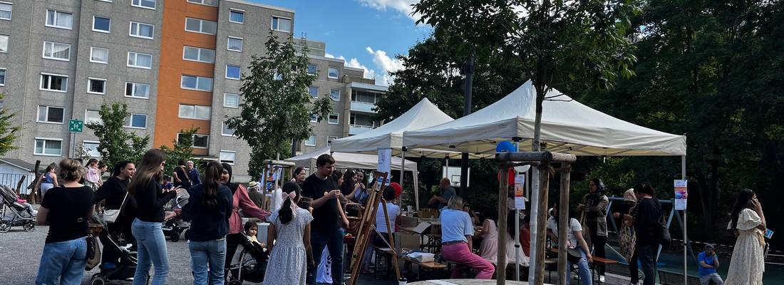 Viele Personen auf einem Fest. Pavillons mit Aktionen zur Teilnahme. Hochhäuser im Hintergrund.