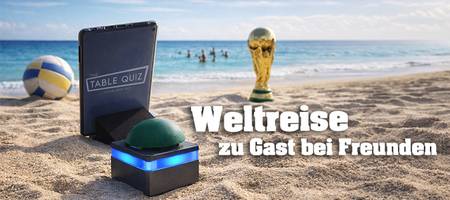 Tablet und Buzzer stehen am Strand vor dem Meer, im Hintergrund sind Menschen im Meer, ein Volleyball und der WM Pokal stehen am Strand