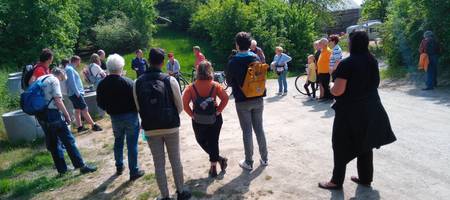 Eine Gruppe von Personen stehend im Kreis, die sich unterhalten. Im Hintergrund grüne Büsche und Gras.
