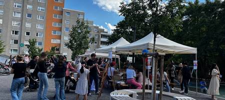 Viele Personen auf einem Fest. Pavillons mit Aktionen zur Teilnahme. Hochhäuser im Hintergrund.