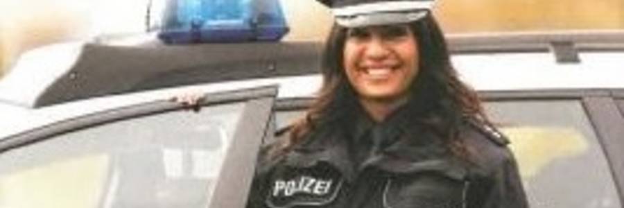 Polizistin mit Migrationshintergrund vor einem Polizeiauto stehend
